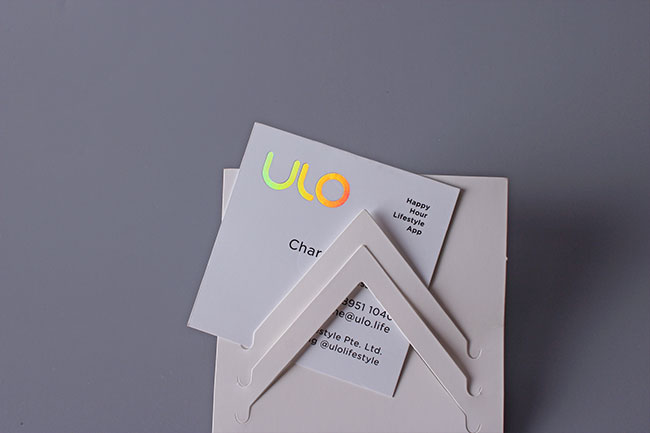 A minimalist white business card featuring a holographic logo and clean sans-serif typography on a display stand.