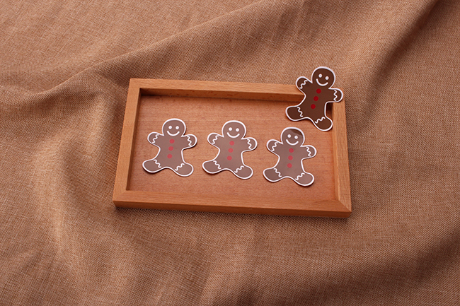 Cute gingerbread man holiday vinyl stickers arranged on a wooden tray.