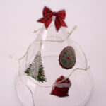 A clear decorative cone wrapped in lights and adorned with festive holiday vinyl stickers.