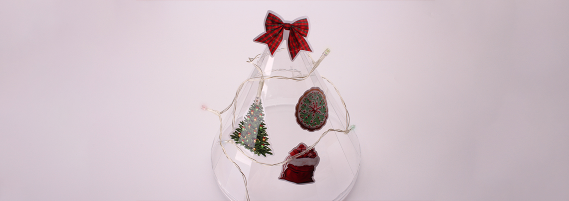 A clear decorative cone wrapped in lights and adorned with festive holiday vinyl stickers.