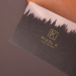 A textured black business card for a photographer featuring gold foil geometric typography and a tree silhouette