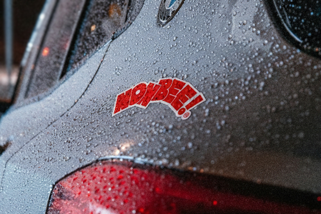 Red "NONBEE!" car sticker with heavy water droplets, illustrating durability for waterproof vs water-resistant needs.