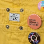 Three social cause button badges pinned to the pocket of yellow denim overalls.