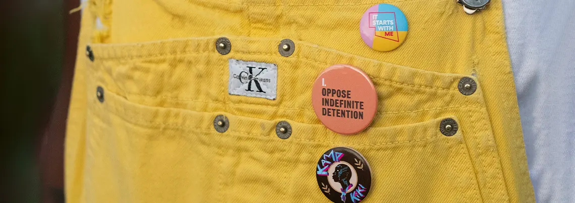 Three social cause button badges pinned to the pocket of yellow denim overalls.
