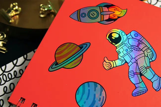 A journal with holographic astronaut and planet stickers on a red cover.