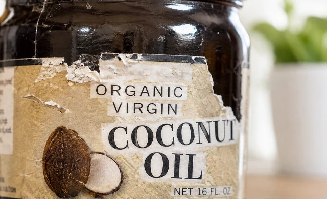 Close-up of a ripped, scuffed, and water-damaged paper label on an organic coconut oil glass jar.